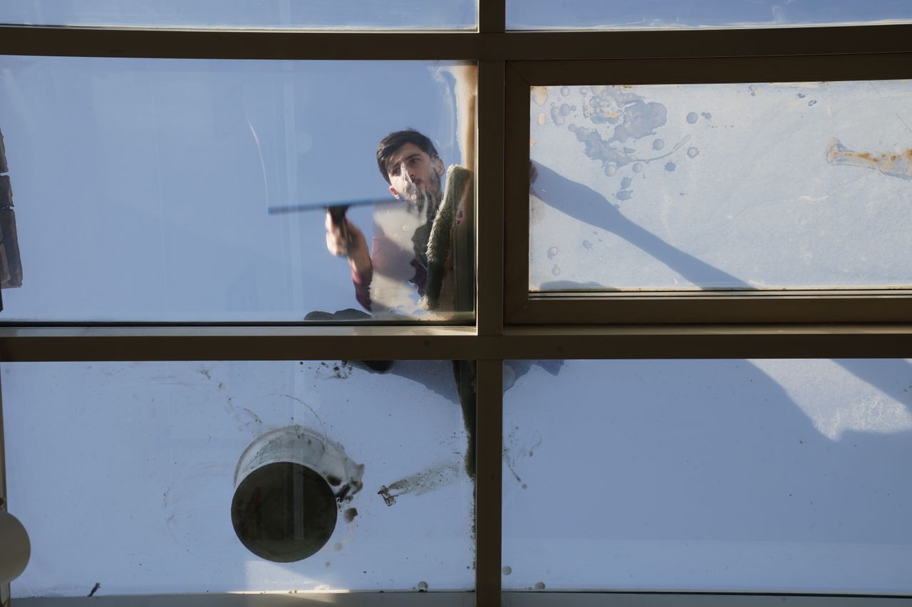 Un nettoyeur de vitres masculin lave la toiture vitrée extérieure par le dessus à l’aide d’un outil pendant la journée.