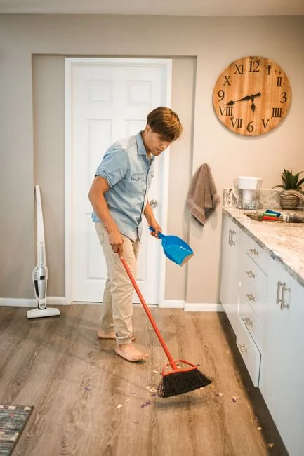 A man cleaning a glass door indoors using a spray bottle and cloth.